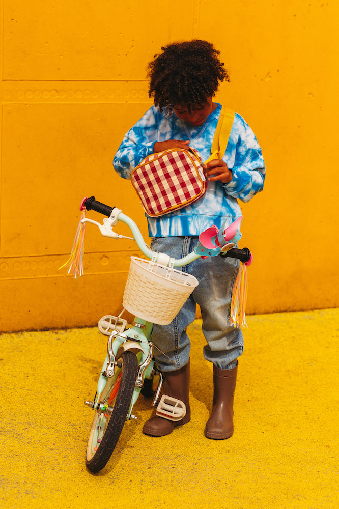 The boy against the yellow wall stands with his bicycle and looks into the giglam red hip pack by bettys home. fanny pack gingham belt bag