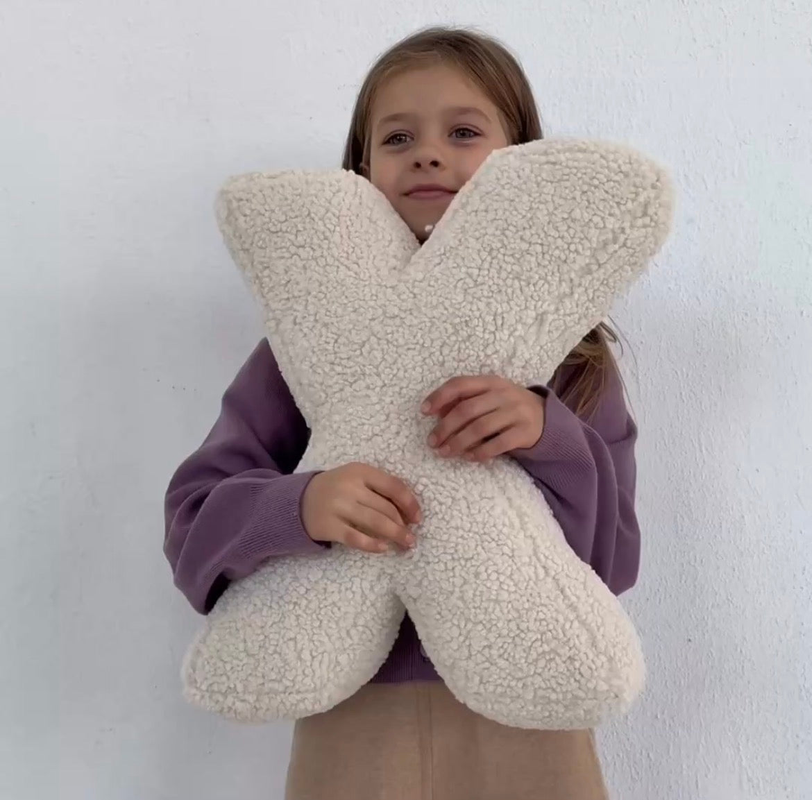 Little girl holding boucle letter cushion X in creme by bettys home