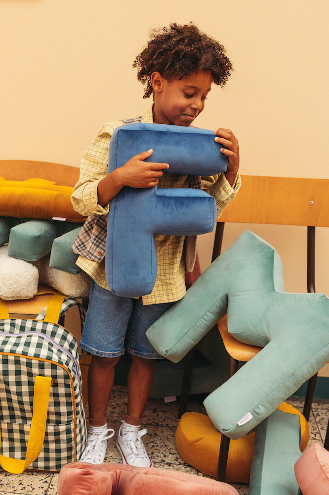 boy at school holding velvet letter cushion F in blue by bettys home. Letter shaped pillows