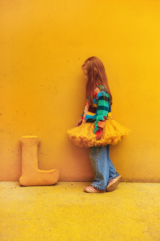 girl in playground against yellow wall stands next to velvet letter cushion L in yellow by bettys home.