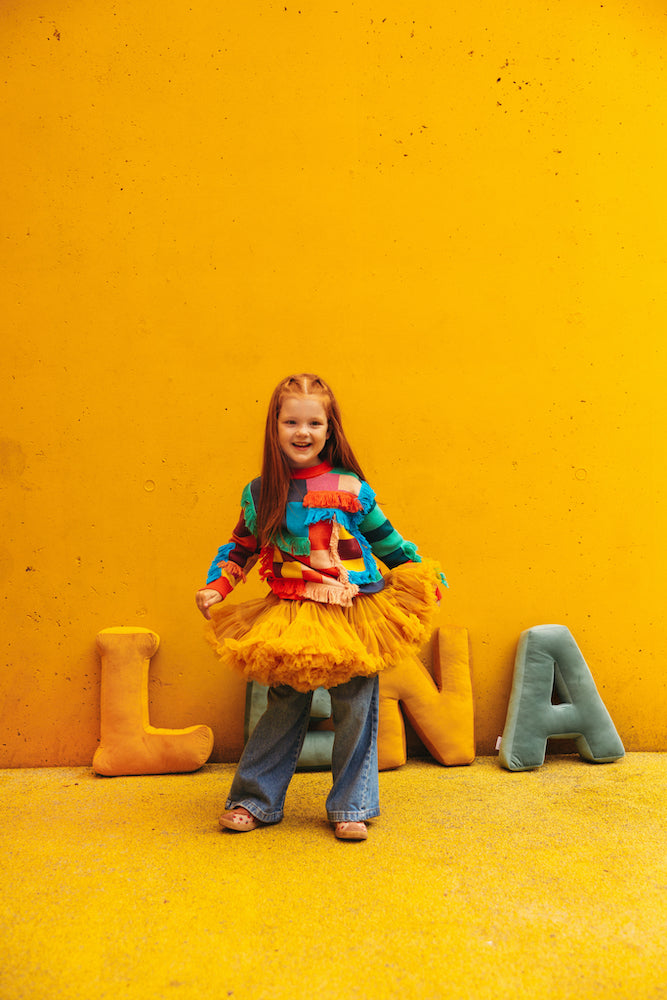 girl in playground against yellow wall stands next to velvet letter cushions L in yellow by bettys home. Velvet pillow