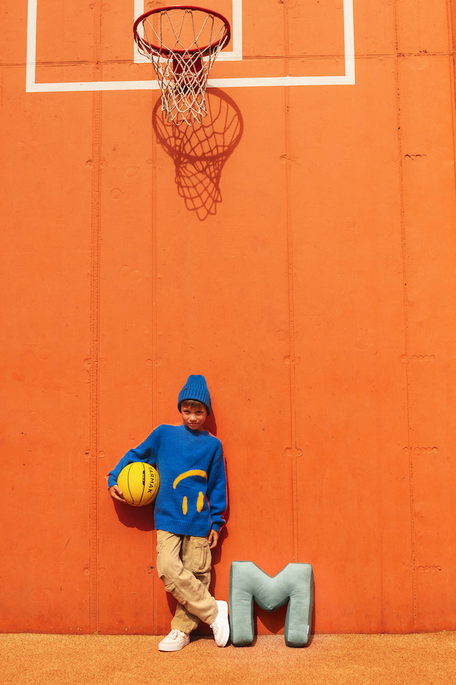 boy in blue blouse on basketball pitch holding ball next to velvet letter cushion M by bettys home.