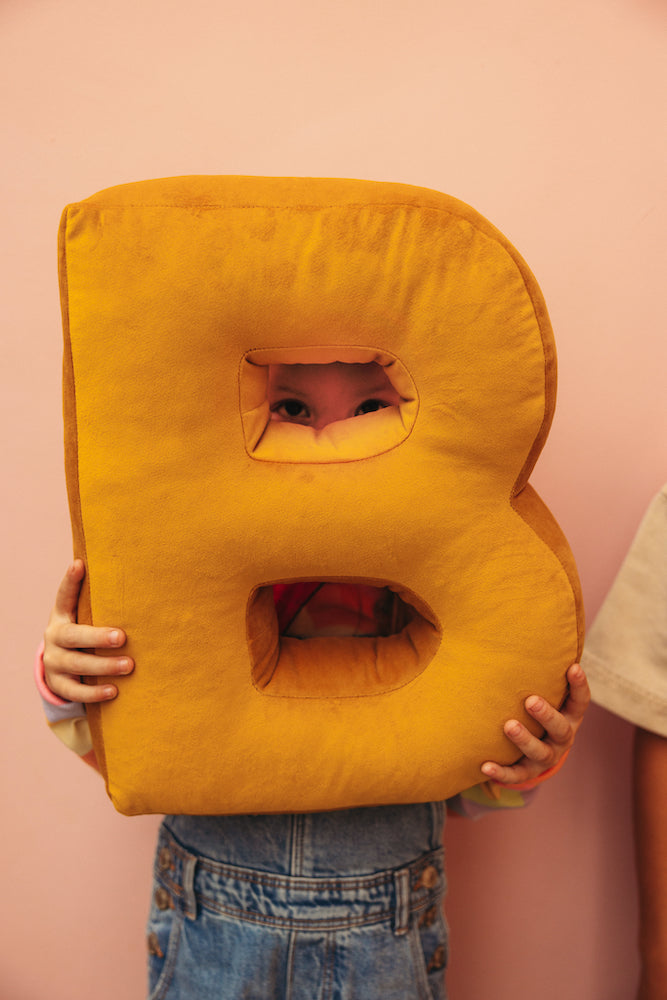 kid holding velvet letter pillow b in yellow by bettys home. letter shaped cushion. 