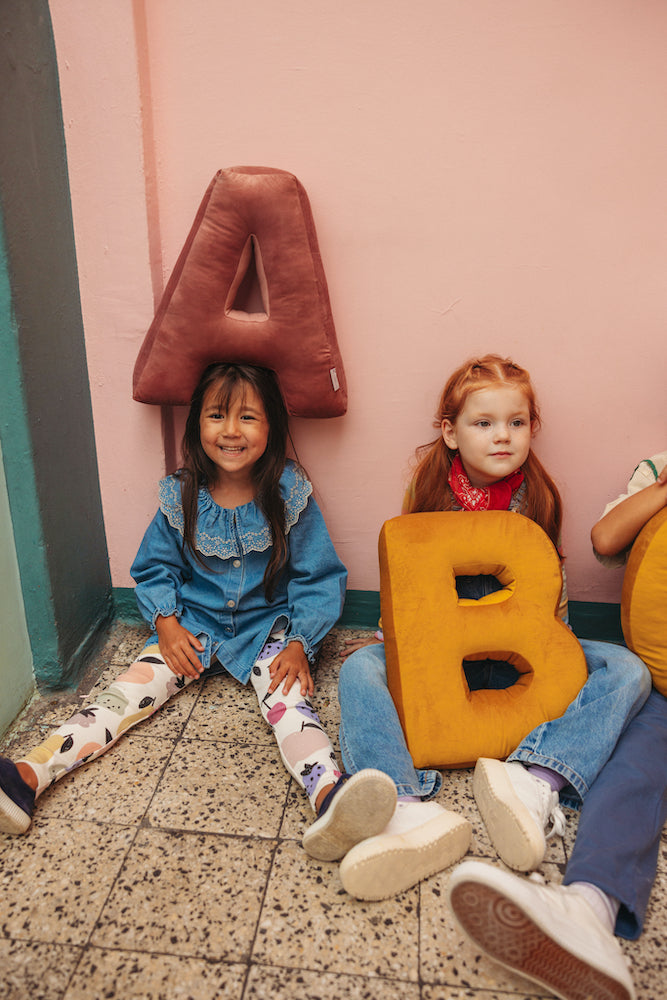 kids at school sitting on floor with velvet letter cushions on head. letter pillow by bettys home